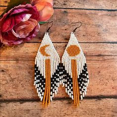 two pairs of beaded earrings sitting on top of a wooden table next to a flower