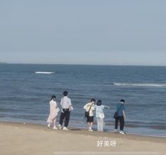 four people standing on the beach looking out at the ocean