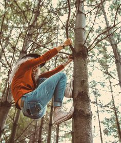 a woman in an orange shirt and jeans climbing up a tree