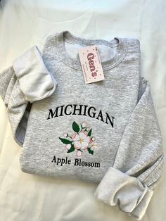 Elevate your style with our Michigan Embroidered Sweatshirt, featuring the state flower, the Apple Blossom, for a trendy touch of local pride. This custom embroidered state sweatshirt is the perfect blend of comfort and style, making it a must-have addition to your wardrobe for showcasing your Michigan love. Color in example is Ash Grey All 50 State Flower Sweatshirts will be available message me if you're looking for a specific one! :) * 50% cotton, 50% polyester * Pre-shrunk * Classic fit * 1x Georgia Flower, Cherokee Rose, Cute Crewneck, Flower Sweatshirt, Sweatshirt Trendy, Magnolia Flower, Embroidered Sweatshirt, Blue Bonnets, Apple Blossom