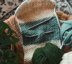 two balls of yarn sitting on top of a woven basket next to some knitting needles