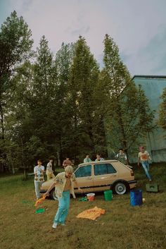 a group of people standing next to a car in a field with trees behind them