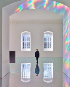 a man standing in front of three windows with rainbow reflections on the floor and walls