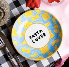 a plate with the word pasta lover written on it next to silverware and flowers