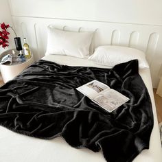 a black blanket is laying on top of a bed with white sheets and pillow cases