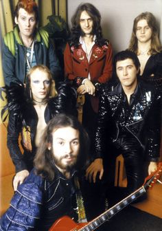 a group of people standing next to each other in front of a wall with guitars