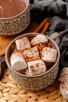 hot chocolate and marshmallows in a bowl with cinnamon sticks on the side