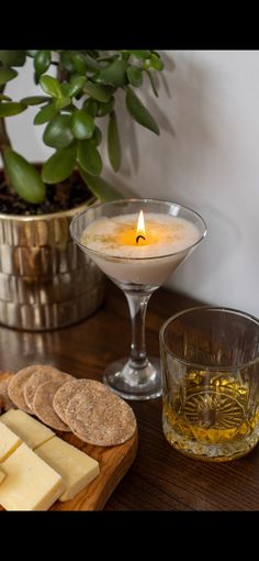 a table topped with wine, crackers and a glass filled with liquid next to a potted plant