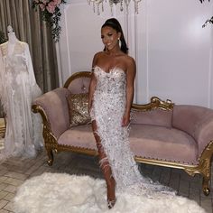 a woman standing in front of a couch wearing a white dress with feathers on it