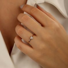 a woman's hand with a diamond ring on her left hand and a white shirt