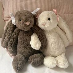 two stuffed animals sitting next to each other on a bed