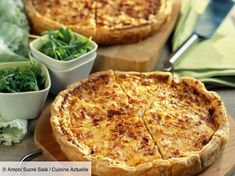 two pizzas sitting on top of a wooden cutting board next to bowls of salad