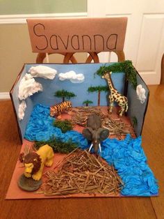 a cardboard box filled with fake animals on top of a wooden floor next to a sign that says savannah