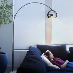 a woman laying on a couch under a lamp next to a potted plant in a living room