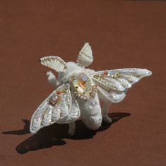 a white stuffed animal with wings and jewels on it's back, sitting on a brown surface