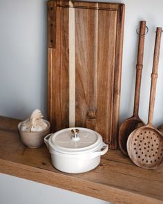 an assortment of cooking utensils on a wooden shelf next to a cutting board