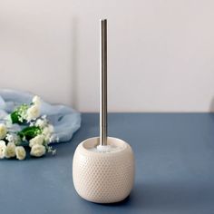 a white toilet brush holder sitting on top of a blue table next to some flowers