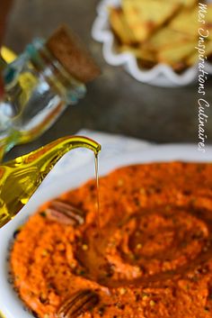 the sauce is being drizzled on top of the dip in a white bowl