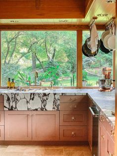 a kitchen with marble counter tops and wooden cabinets in front of a large window that has pans hanging from the ceiling