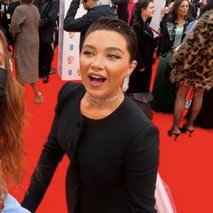 two women standing on a red carpet with their mouths open and people in the background