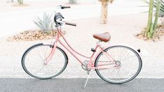 a pink bike is parked on the side of the road next to a cactus tree