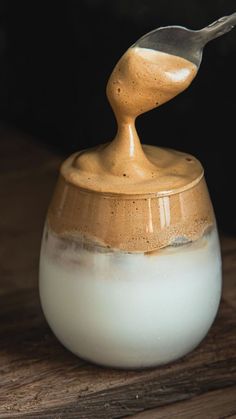 a spoon sticking out of a jar filled with liquid on top of a wooden table