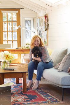 a woman sitting on top of a couch holding a black dog in her lap and smiling at the camera