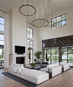 a living room filled with white furniture and large windows next to a fire place on top of a hard wood floor