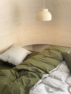 an unmade bed with green sheets and pillows in a room that has a lamp hanging above it