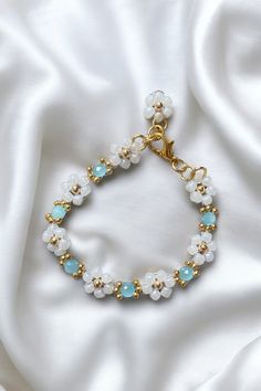 Coastal Breeze Daisy Chain Bracelet - 18K Gold-Plated, Aqua Blue Gem & White Glass Flower, Adjustable Chain, Gift for Her Add a touch of serene elegance to your jewellery collection with the Coastal Breeze Daisy Chain Bracelet, a beautiful piece that blends luxury with refreshing colour. Featuring delicate white glass flowers arranged in a daisy chain design, each flower is centred with shimmering 18K gold-plated beads and complemented by a vibrant aqua blue gem. This bracelet brings a sophistic Light Blue Beaded Flower Jewelry, Adjustable White Jewelry With Flower Decoration, Light Blue Flower-shaped Beaded Jewelry, Delicate White Flower Bracelets, Handmade White Crystal Bracelet With Flower Shape, Handmade White Crystal Bracelet In Flower Shape, Handmade White Crystal Flower Bracelet, White Flower-shaped Wedding Bracelets, Adjustable White Bracelet With Flower Decoration