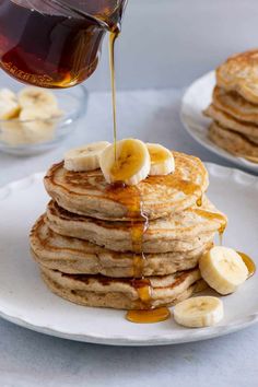 a stack of pancakes with syrup being drizzled over them and sliced bananas