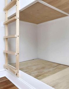 an empty room with white walls and wooden shelves on the bottom floor, next to a ladder