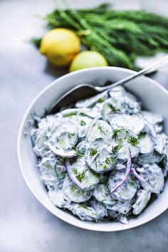 a white bowl filled with cucumber salad next to lemons and green onions