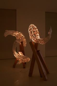 two sculptures made out of wood and paper with lights on them in the shape of fish tails