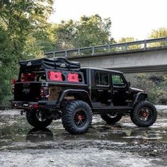 a black jeep parked on the side of a river with a bridge in the background