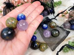 a person holding several different colored stones in their hand next to some plants and flowers