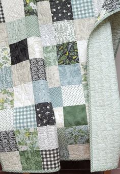 a green and white quilt sitting on top of a wooden table next to a chair