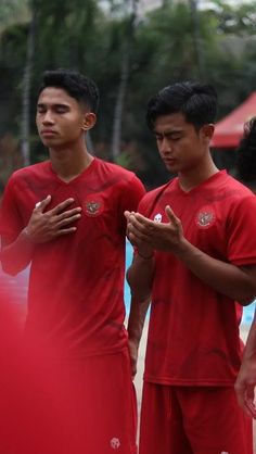 three men in red soccer uniforms standing next to each other and looking at their cell phones