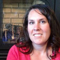 a woman in a red shirt is smiling at the camera with a fireplace behind her