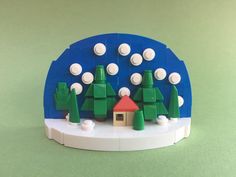 a toy house with trees and snow around it on top of a green tablecloth