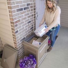 a woman unpacking boxes in front of a brick building with purple flowers on the ground