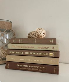 a stack of books sitting on top of a white table next to a glass vase