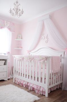 a white crib with pink bedding and a chandelier