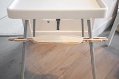 a close up of a white highchair with wooden seat and back rests on the floor