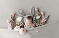 a baby is sleeping with flowers and bunny ears on it's head in a white blanket