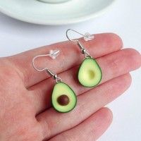 an avocado shaped earrings is being held in someone's hand with a cup and saucer behind it