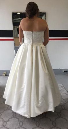 a woman in a white wedding dress looking at herself in the mirror with her back to the camera