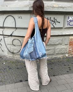 a woman is standing on the sidewalk with her back to the camera and holding a blue bag