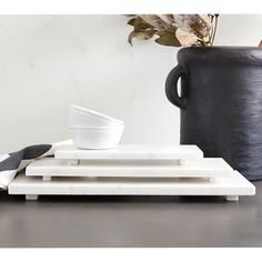 a white bowl sitting on top of a wooden tray next to a black vase with flowers in it