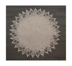 a white doily with leaves on it sitting on top of a wooden table next to a wall